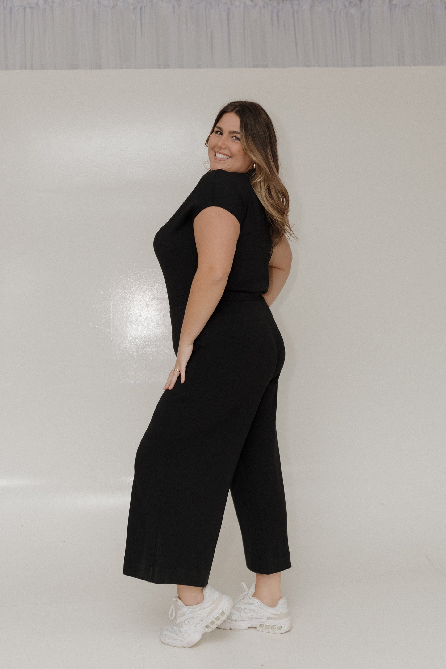 Woman wearing a black outfit with wide-leg pants against a white background