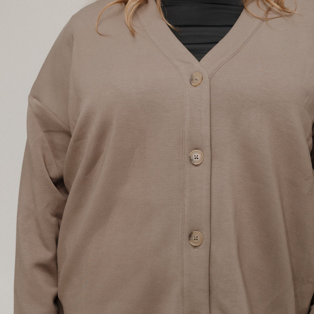 Person wearing a brown cardigan over a black shirt on a plain background