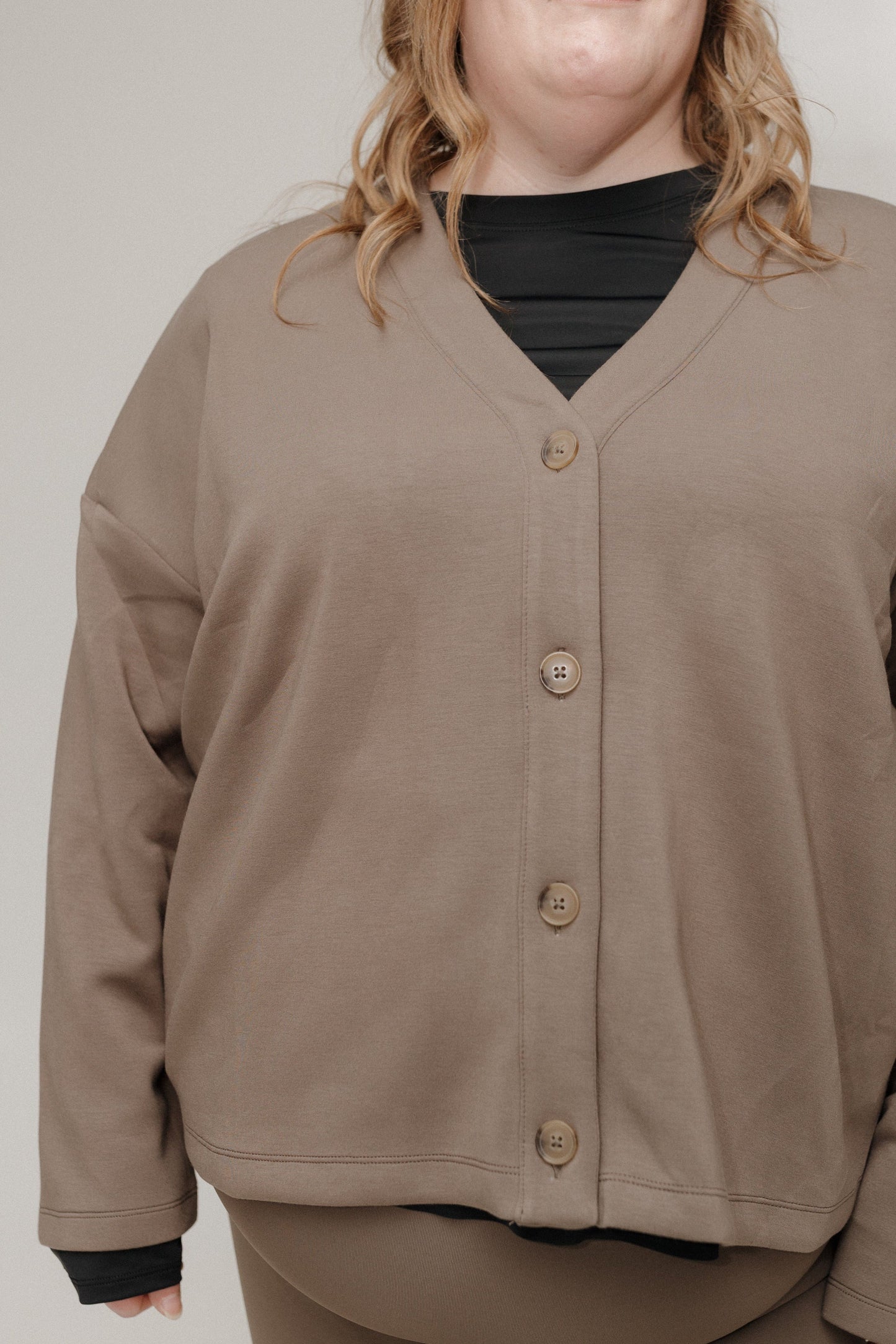 Person wearing a brown cardigan over a black shirt on a plain background