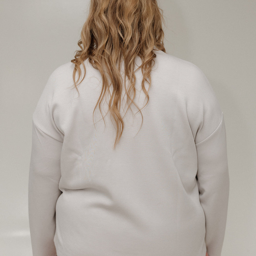Person wearing a light gray sweater and pink pants against a plain background