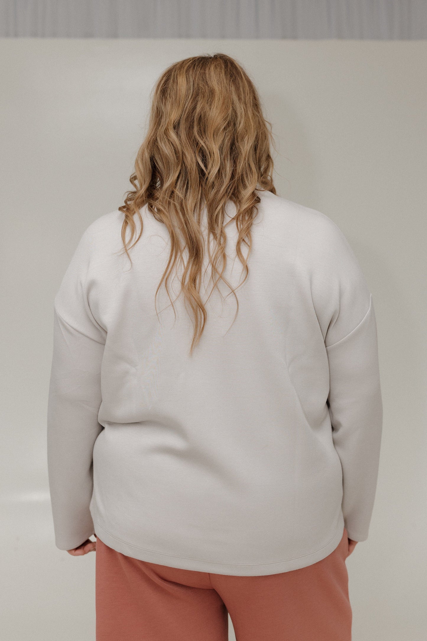 Person wearing a light gray sweater and pink pants against a plain background