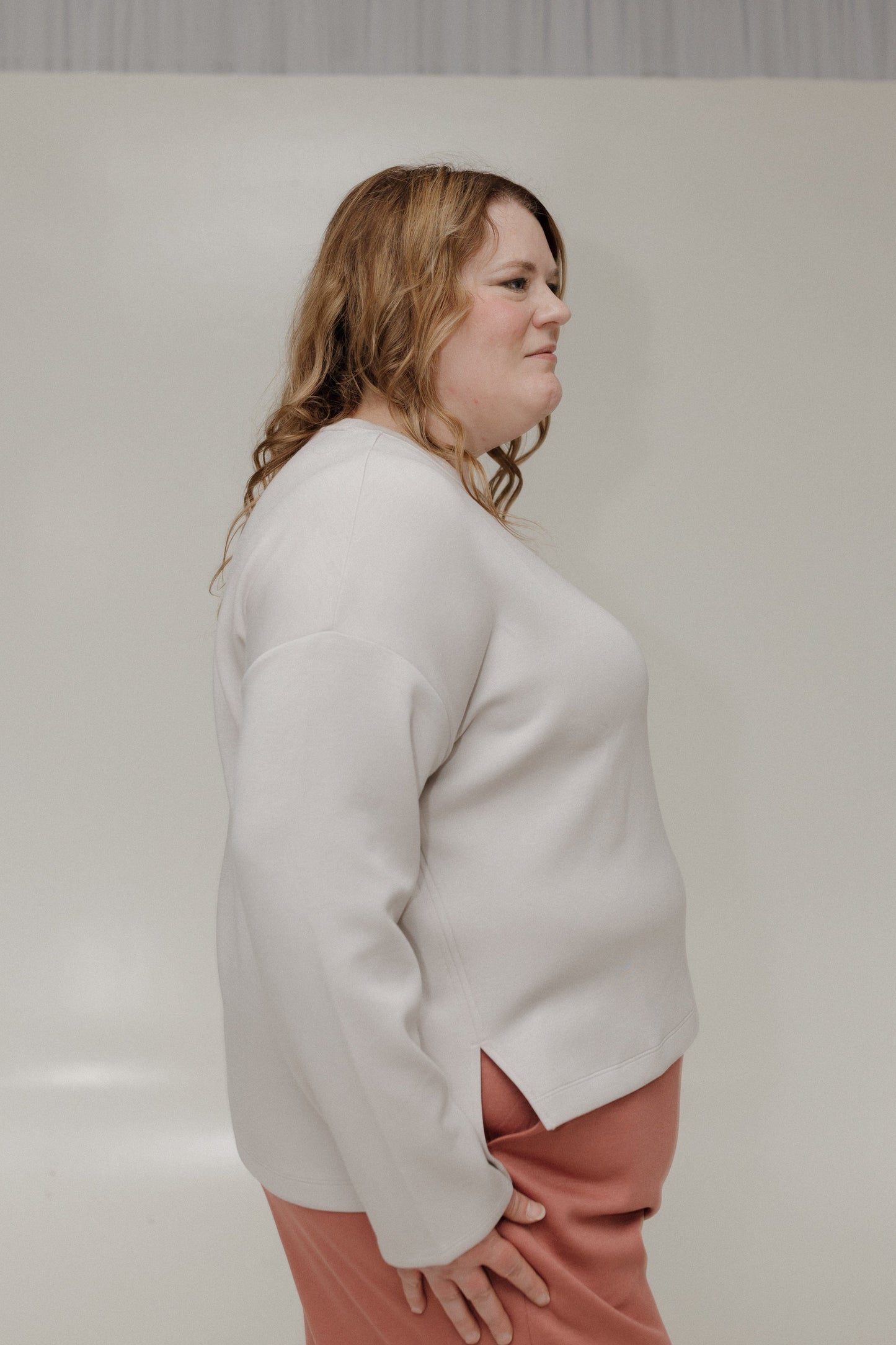 Woman wearing a light gray sweater and pink pants against a plain background