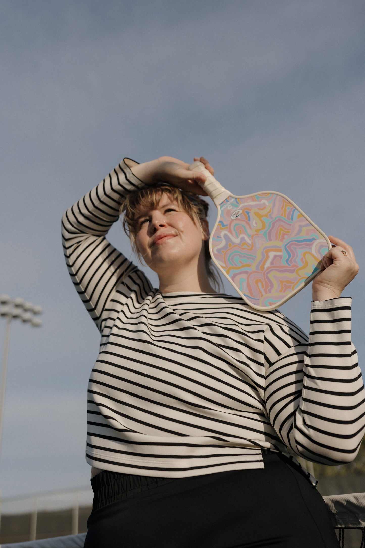 Person holding a colorful paddle against a cloudy sky