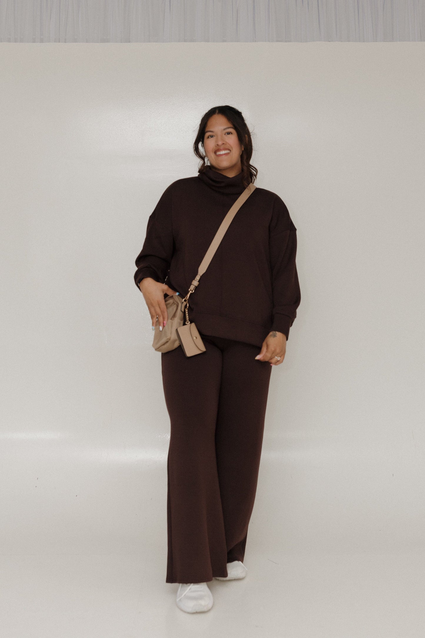 Person wearing a brown outfit with a beige bag on a white background