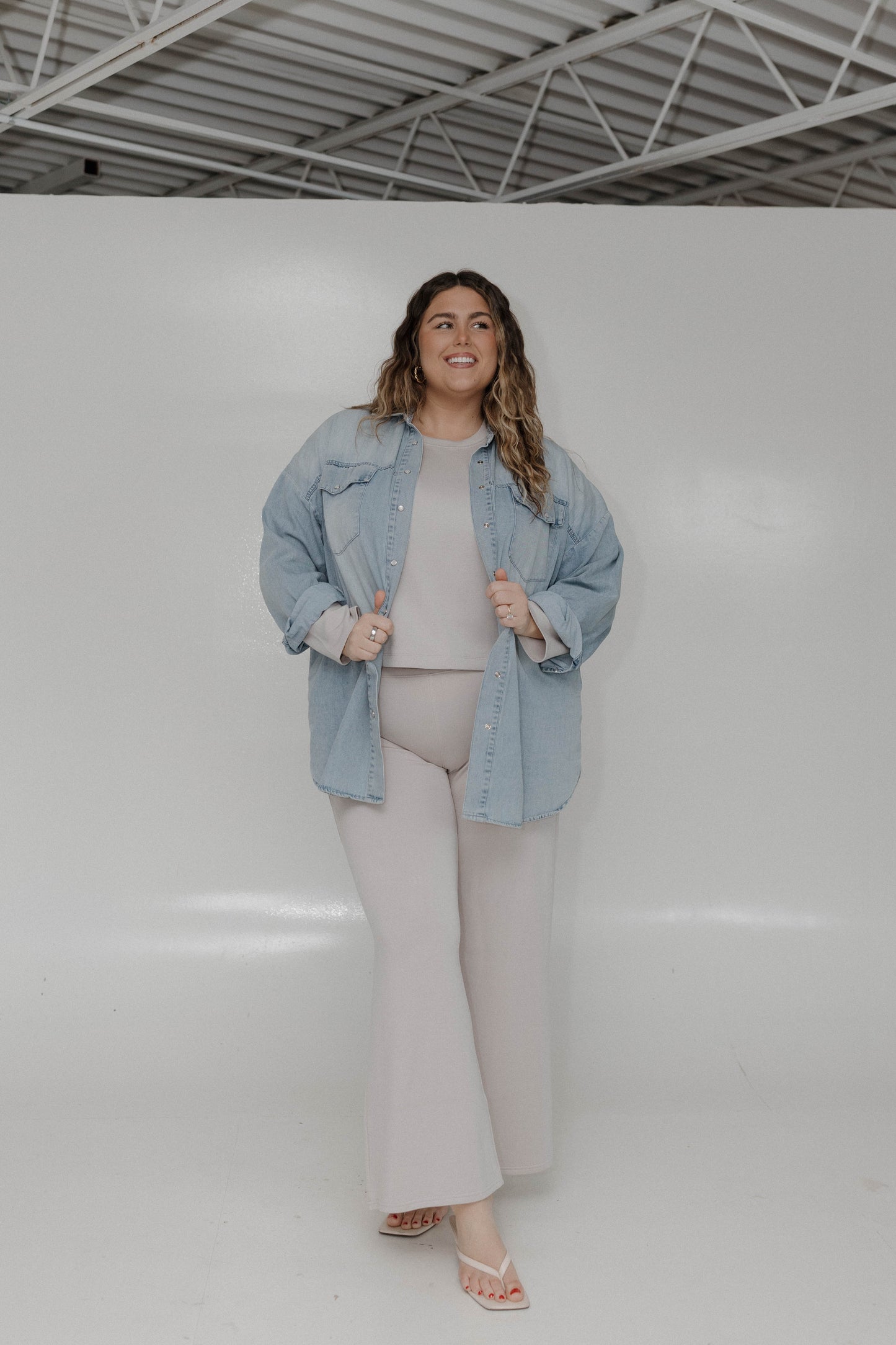 Woman wearing a denim jacket and light-colored pants in a studio setting