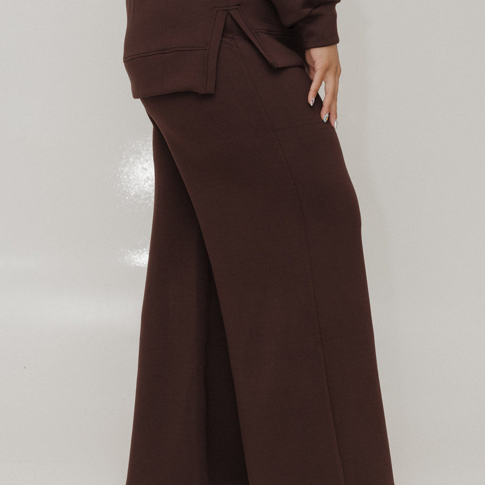 Person wearing a brown suit with wide-leg pants on a white background