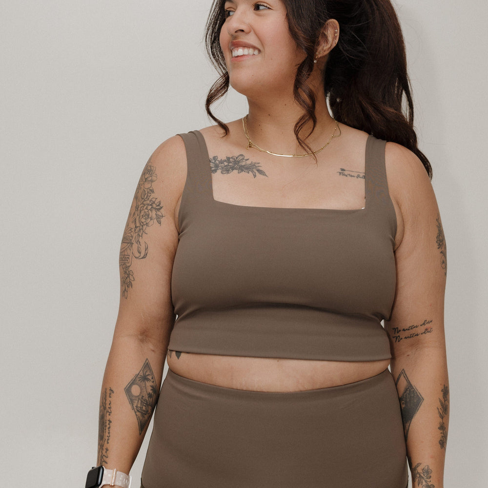 Woman wearing a brown tank top and leggings against a plain background