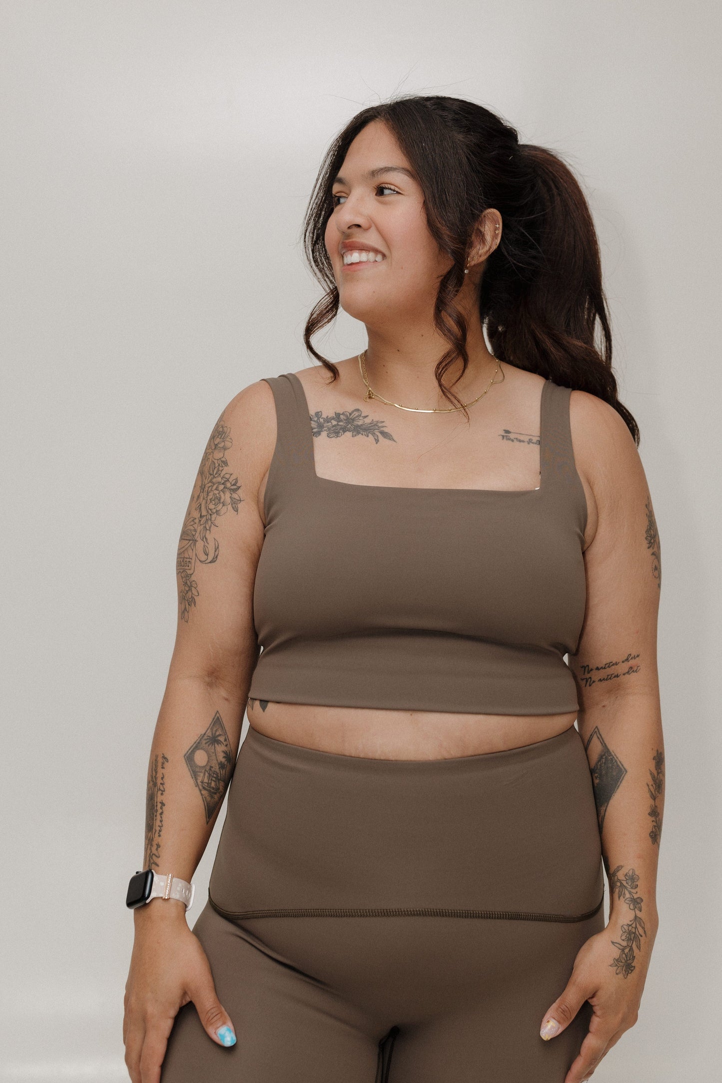 Woman wearing a brown tank top and leggings against a plain background