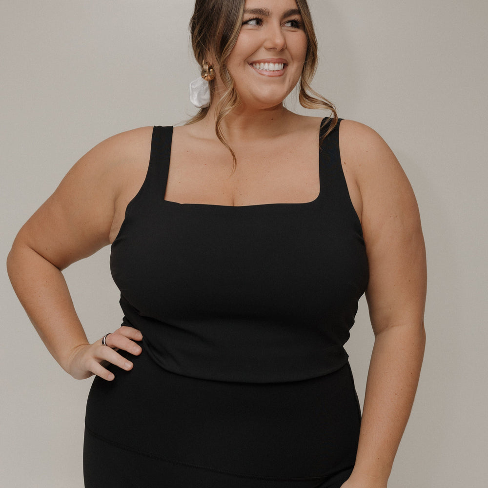 Woman wearing a black tank top and black pants against a plain background