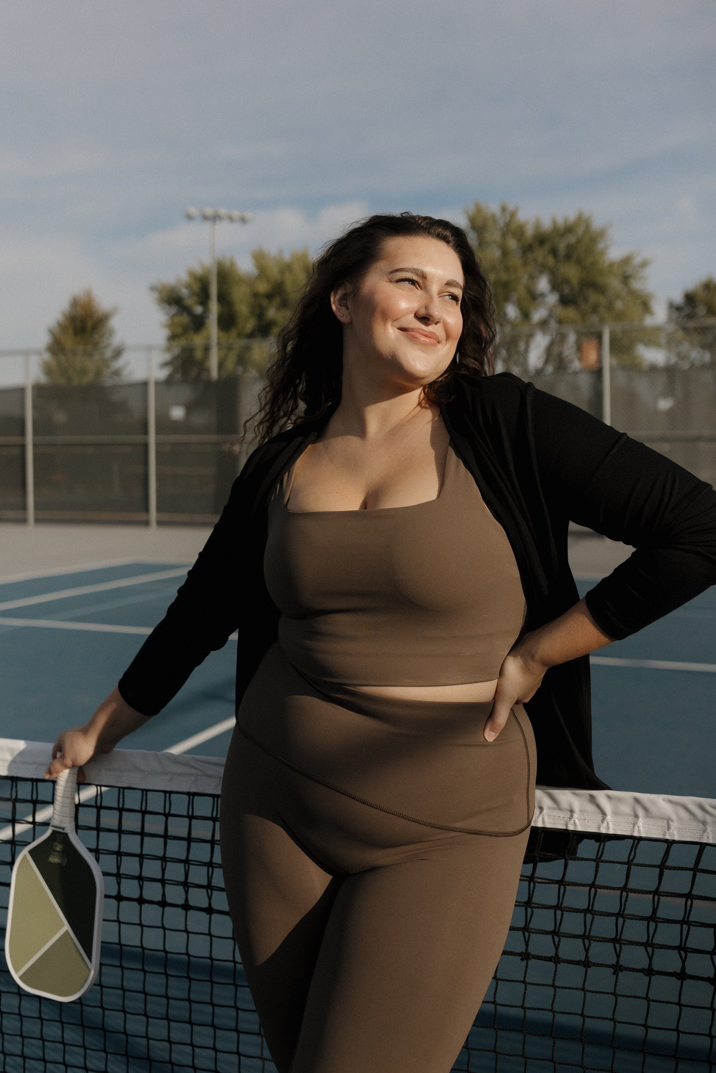 Woman in brown athletic wear standing on a tennis court with a racket.