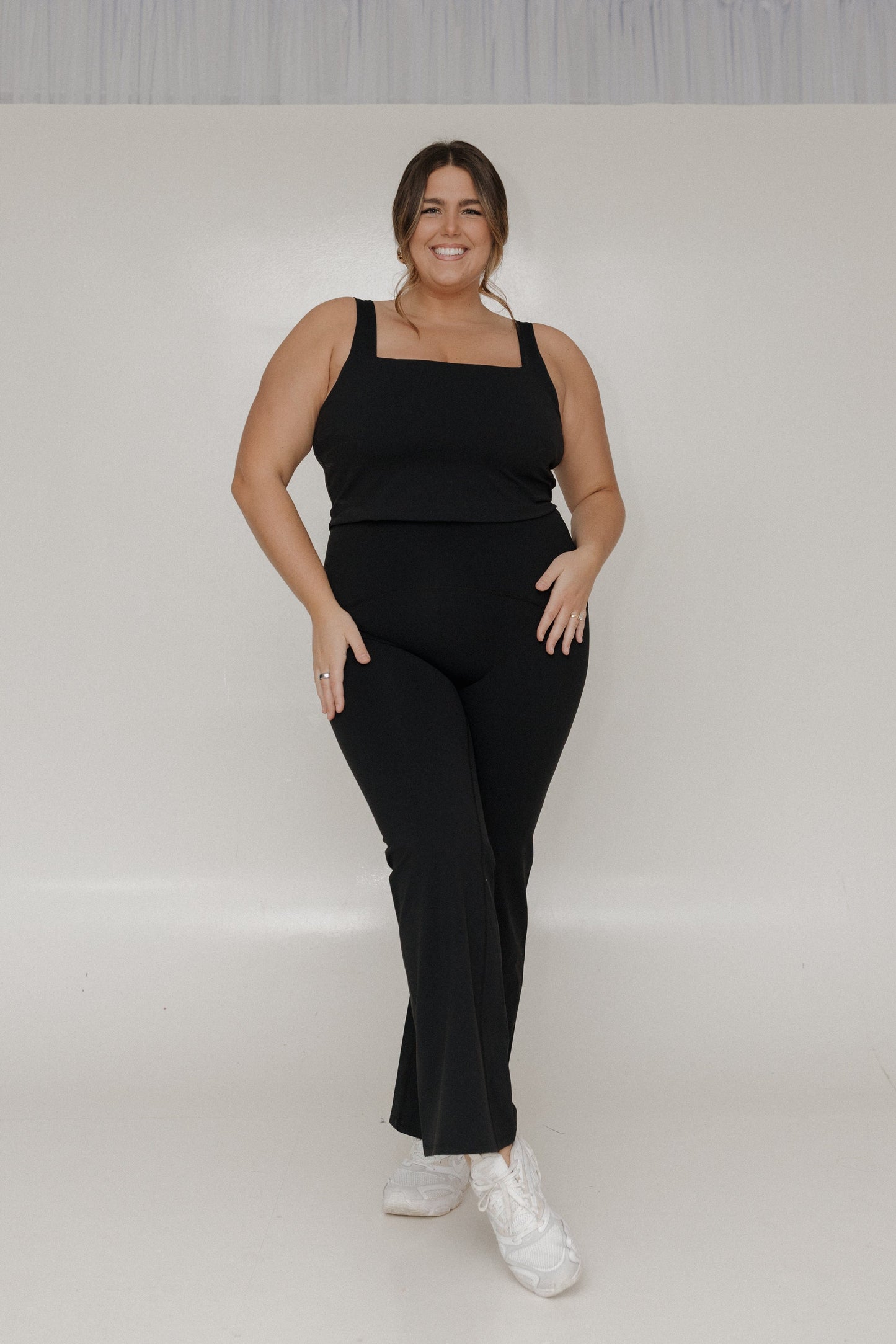 Woman wearing a black outfit with white sneakers on a plain background