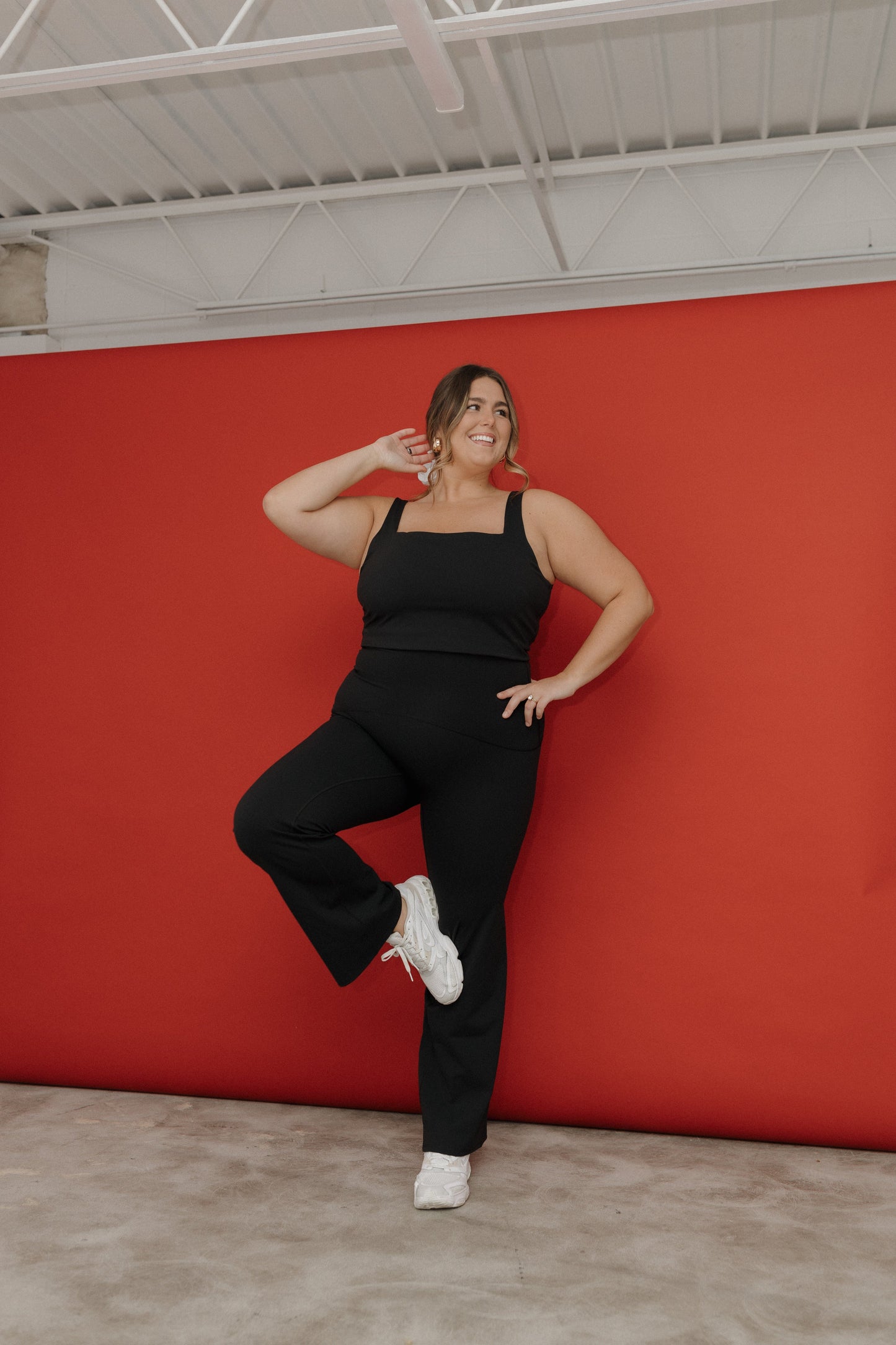 Woman in black outfit posing against a red wall