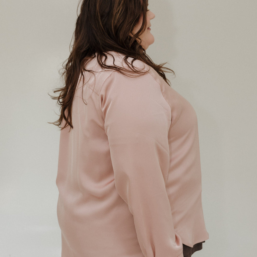 Person wearing a light pink shirt and blue jeans against a plain background