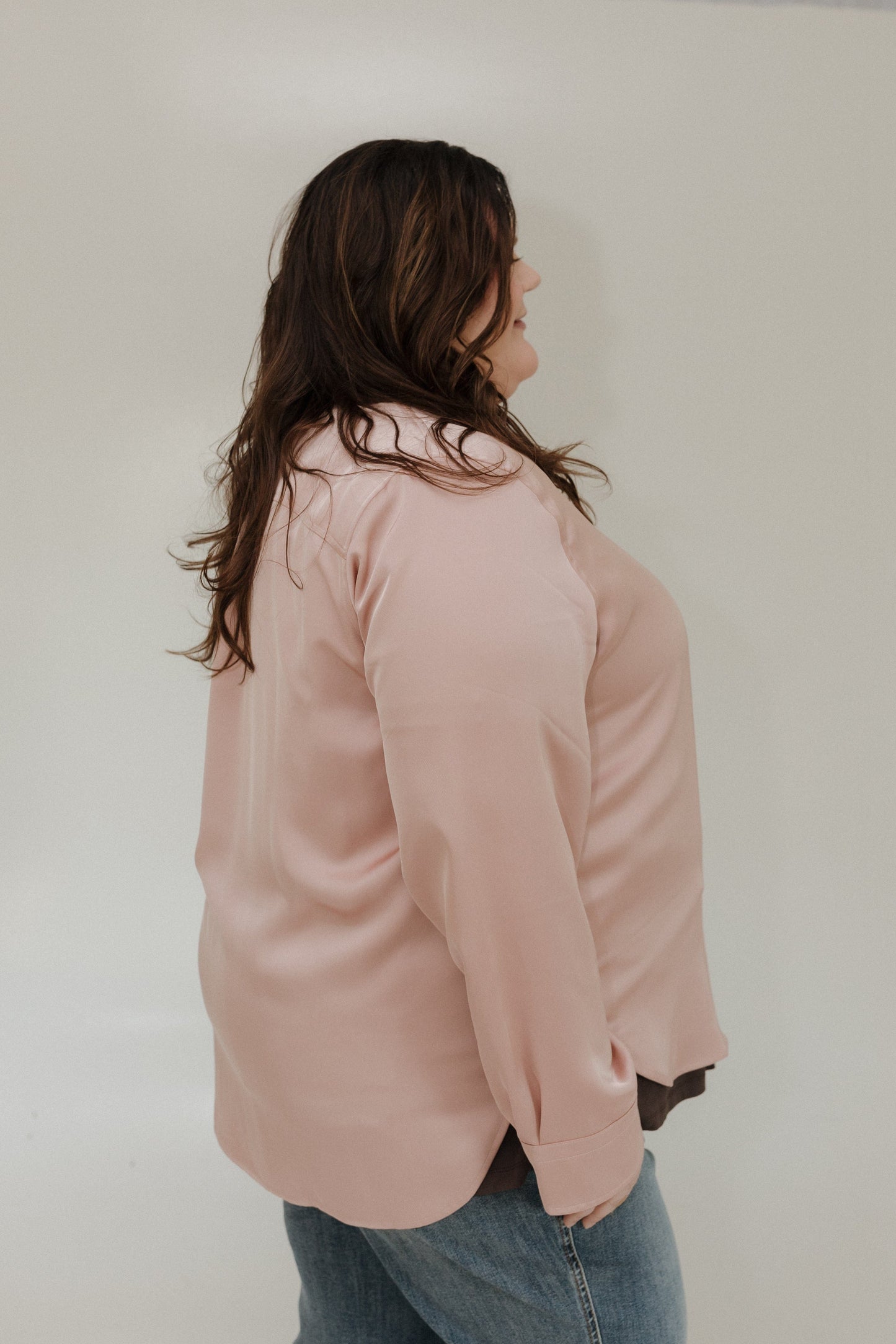 Person wearing a light pink shirt and blue jeans against a plain background