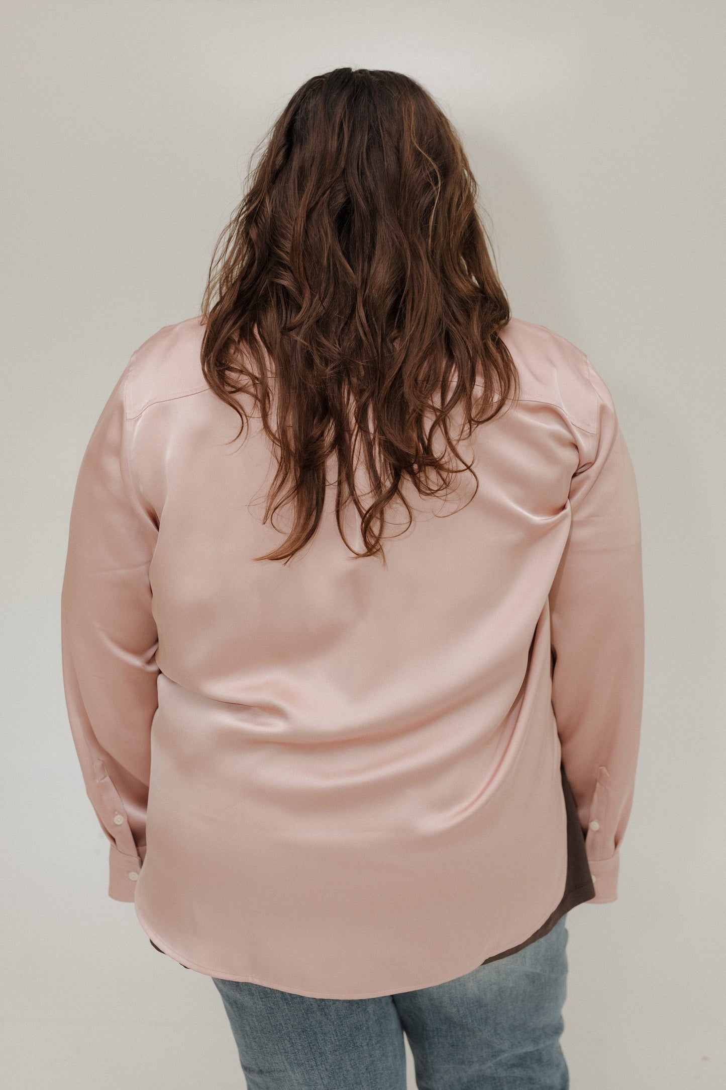 Person wearing a light pink satin shirt with a plain background