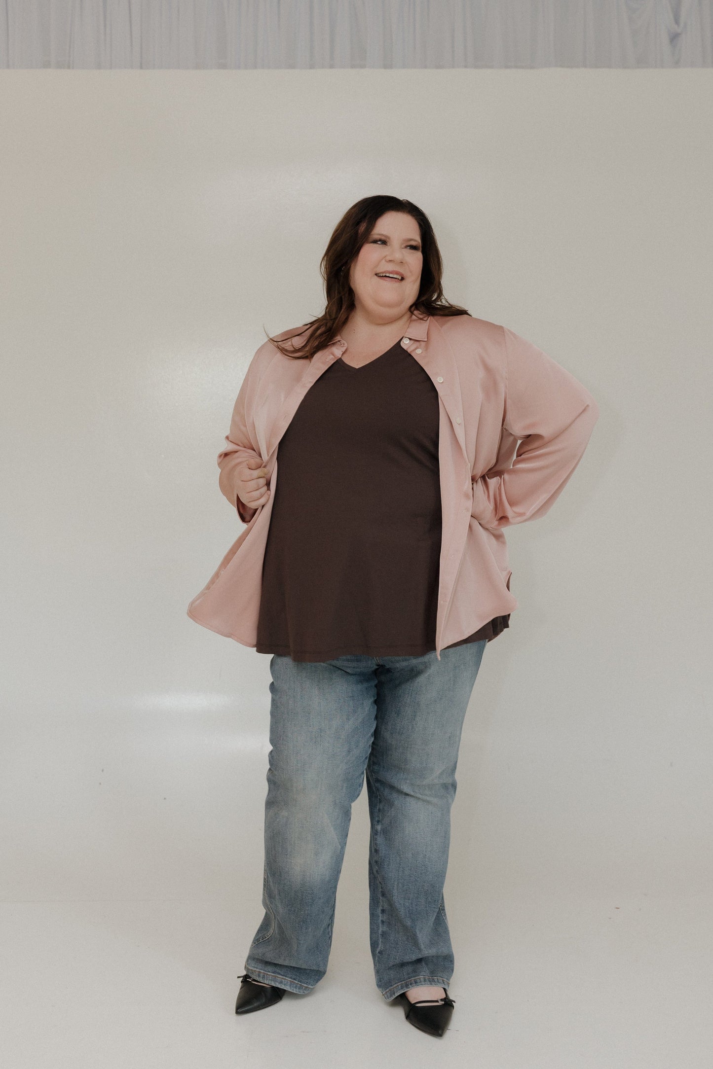 Woman wearing a pink jacket, brown shirt, and blue jeans on a white background