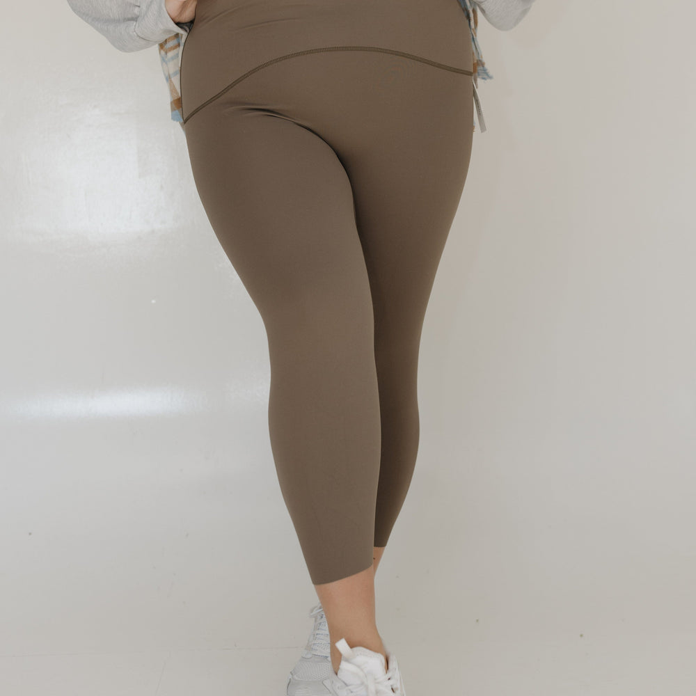Person wearing brown leggings and white sneakers on a plain background