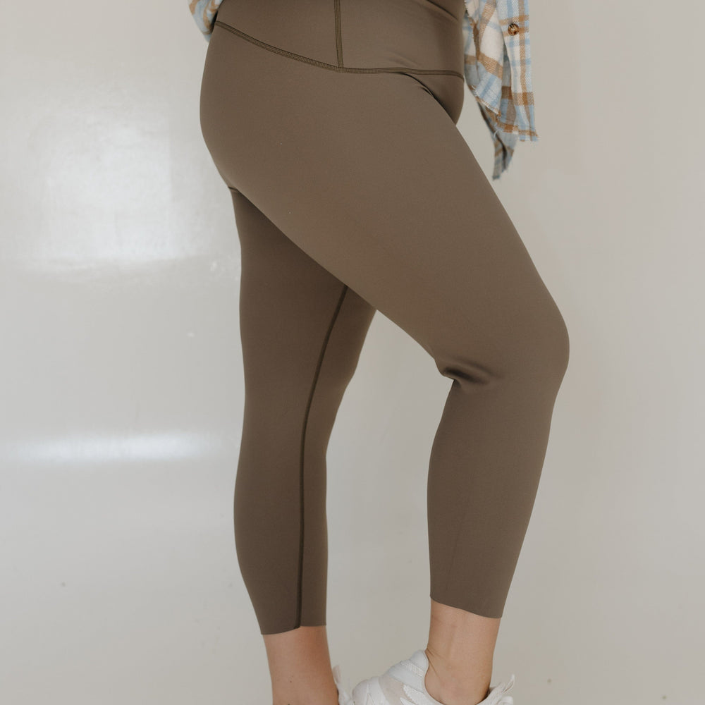 Person wearing brown leggings and white sneakers on a plain background