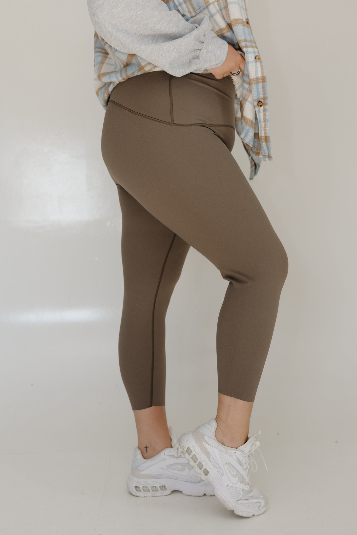 Person wearing brown leggings and white sneakers on a plain background