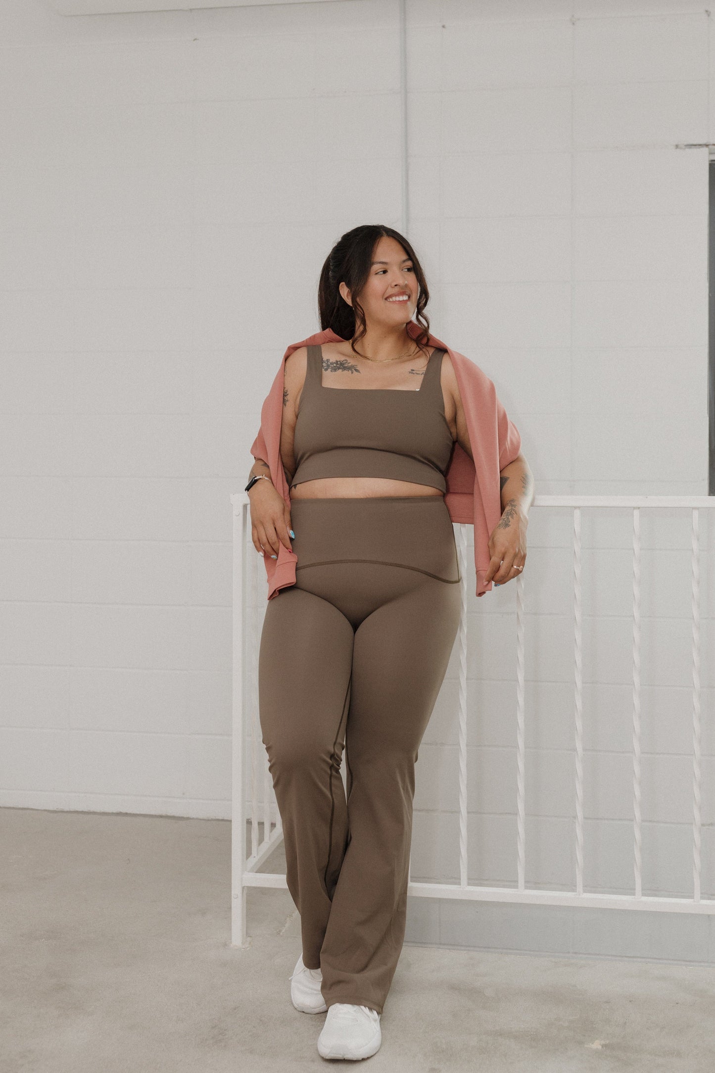 Woman wearing a brown outfit with a pink cardigan against a white wall.