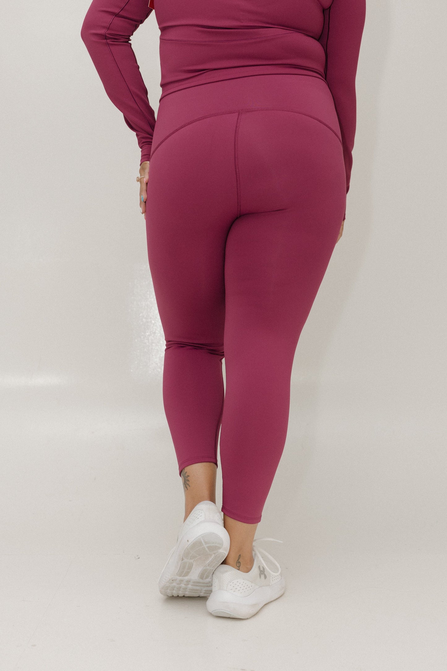 Person wearing magenta leggings and top on a white background