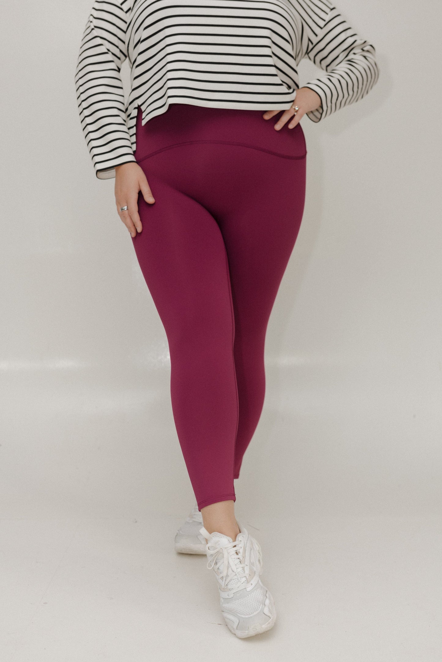 Person wearing maroon leggings and a striped sweater on a white background