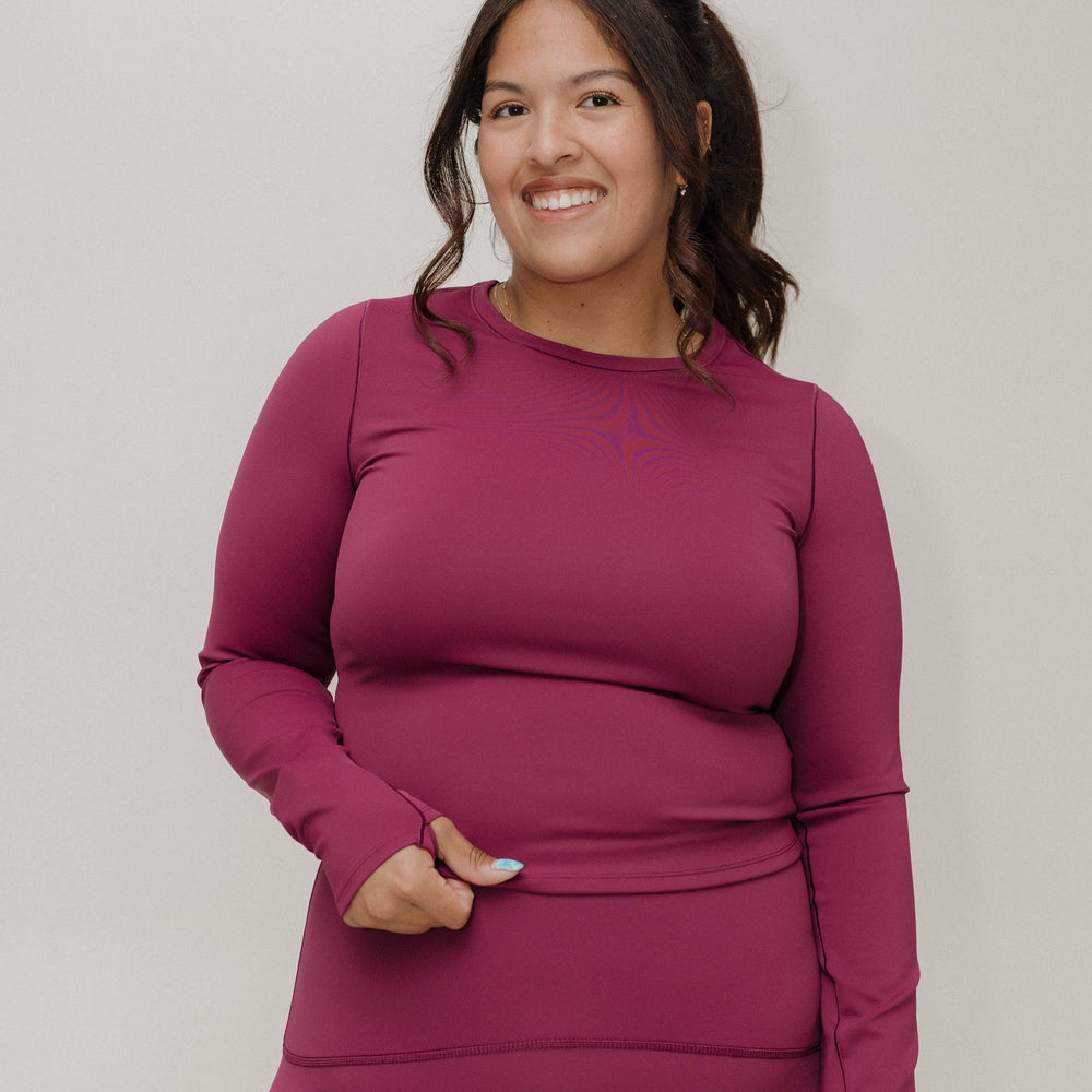 Woman wearing a magenta long-sleeve top and pants against a plain background