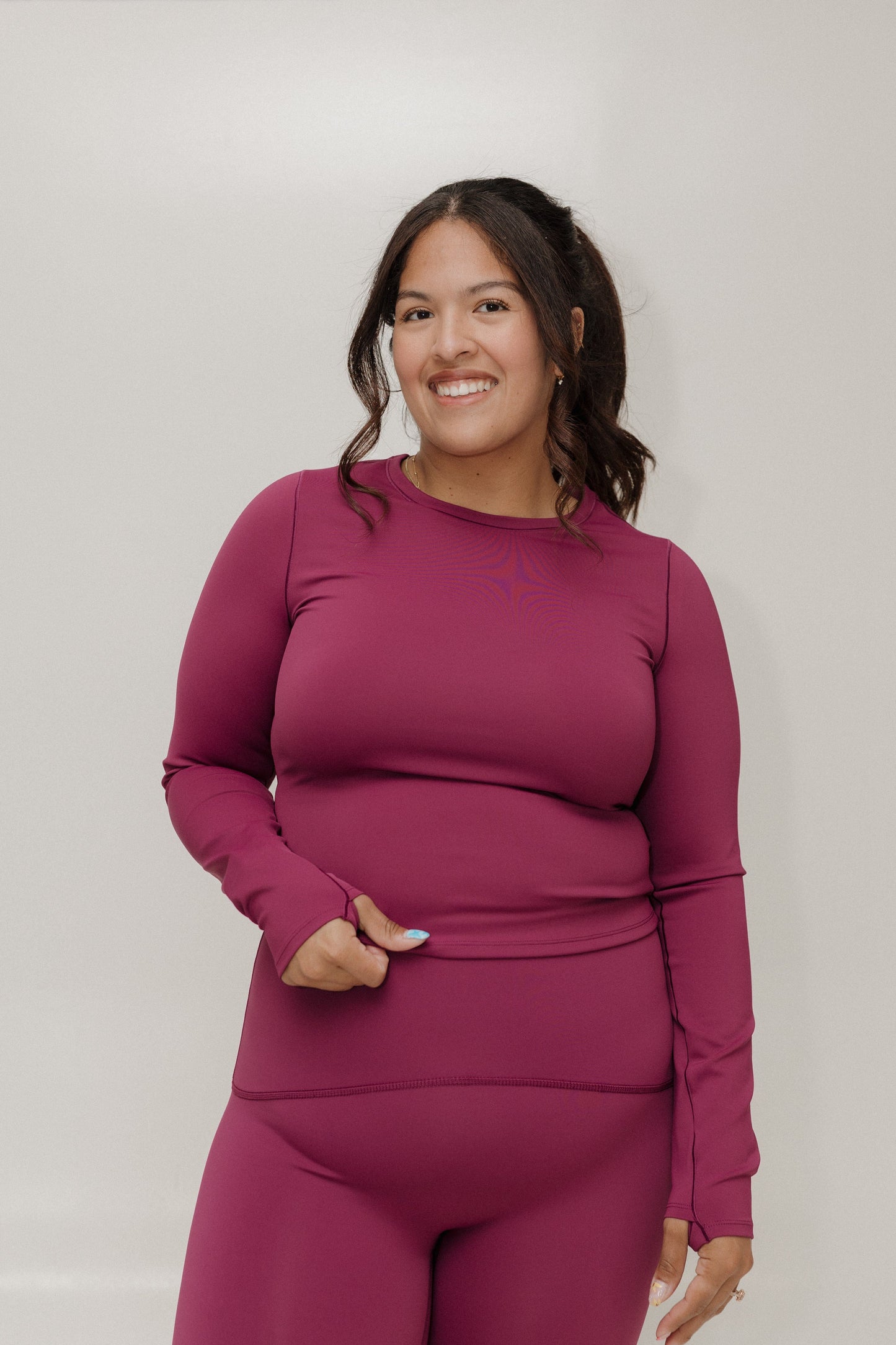 Woman wearing a magenta long-sleeve top and pants against a plain background