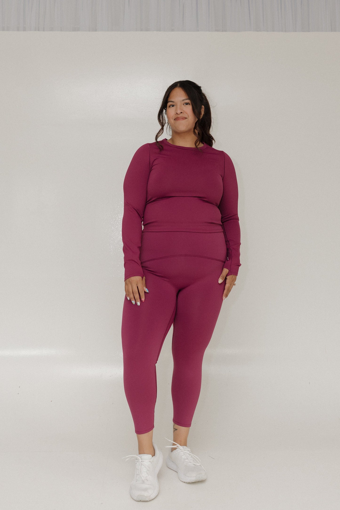 Woman wearing a magenta outfit with white sneakers on a plain background