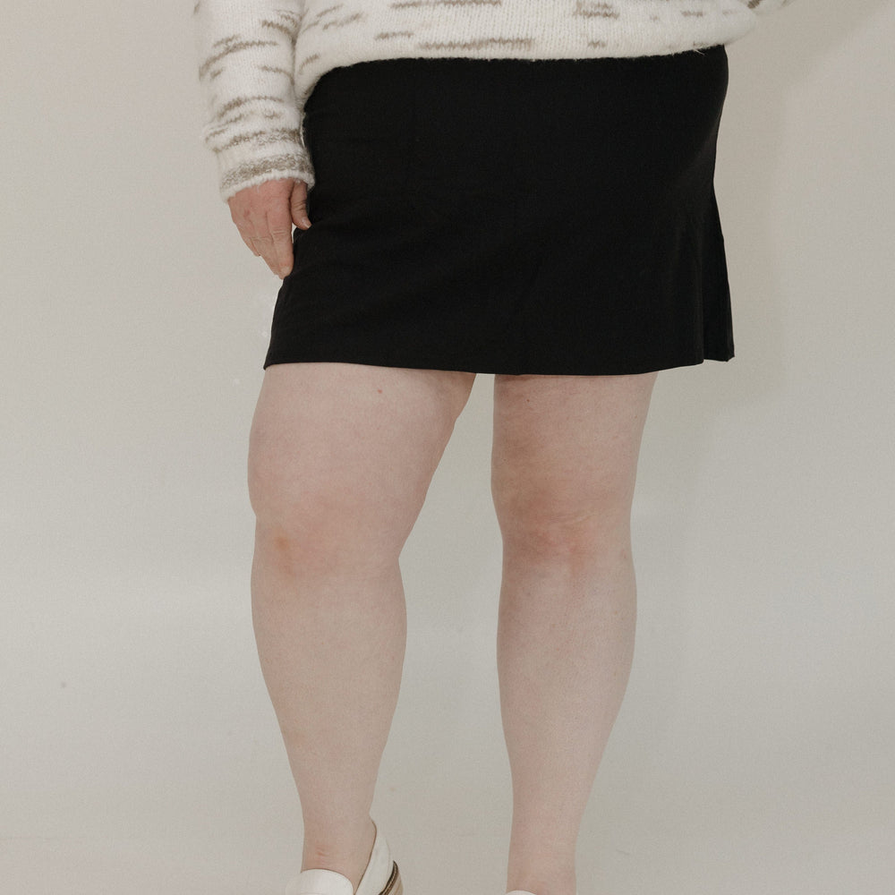 Person wearing a black skirt and white sneakers on a plain background