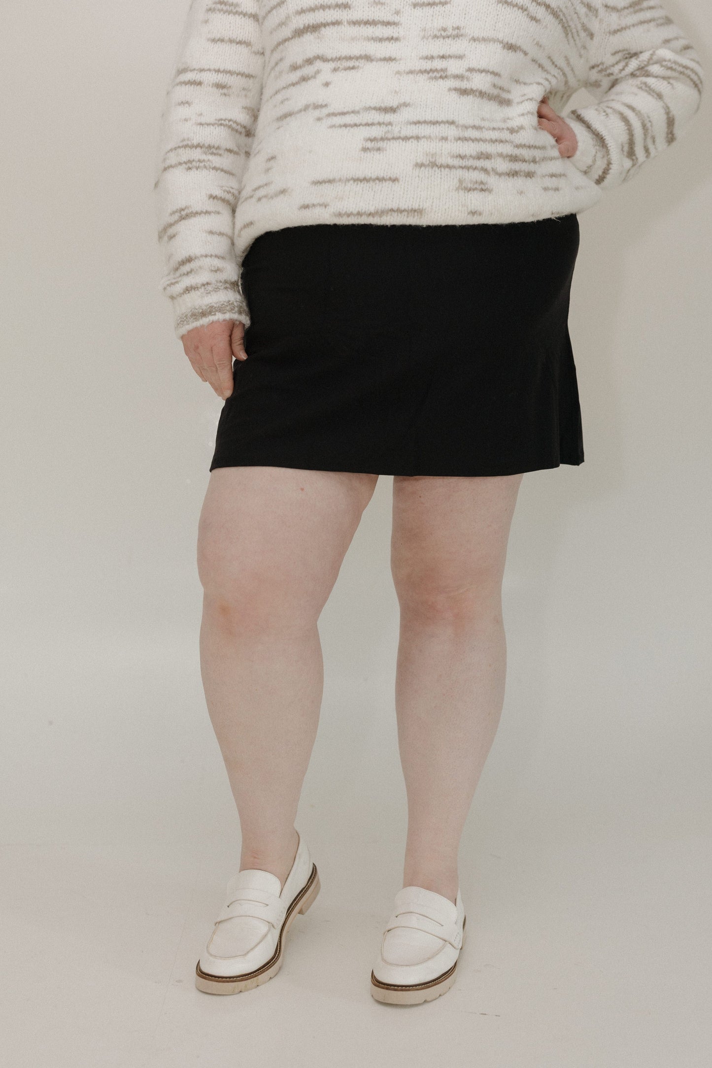 Person wearing a black skirt and white sneakers on a plain background