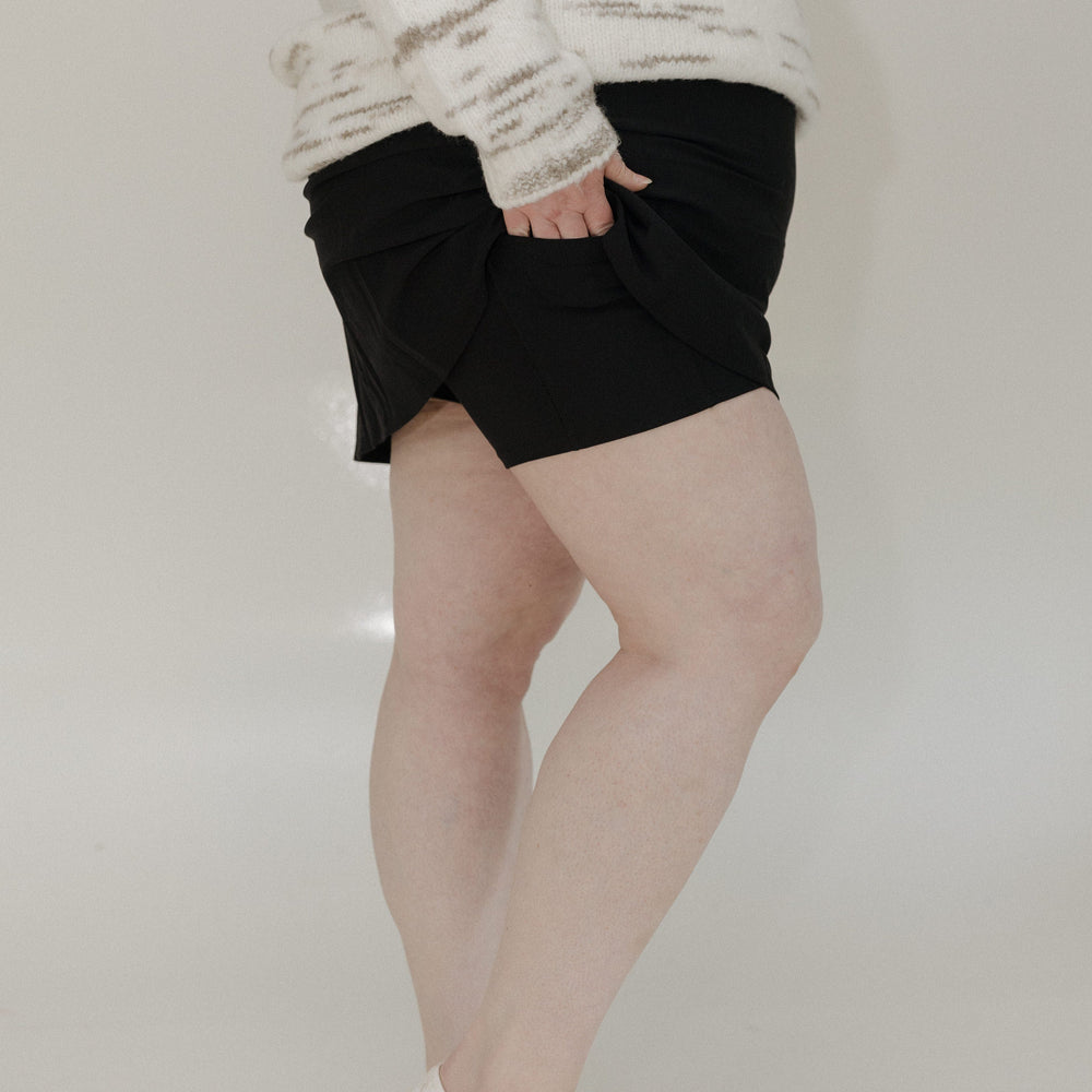 Person wearing a white sweater, black shorts, and white shoes on a plain background