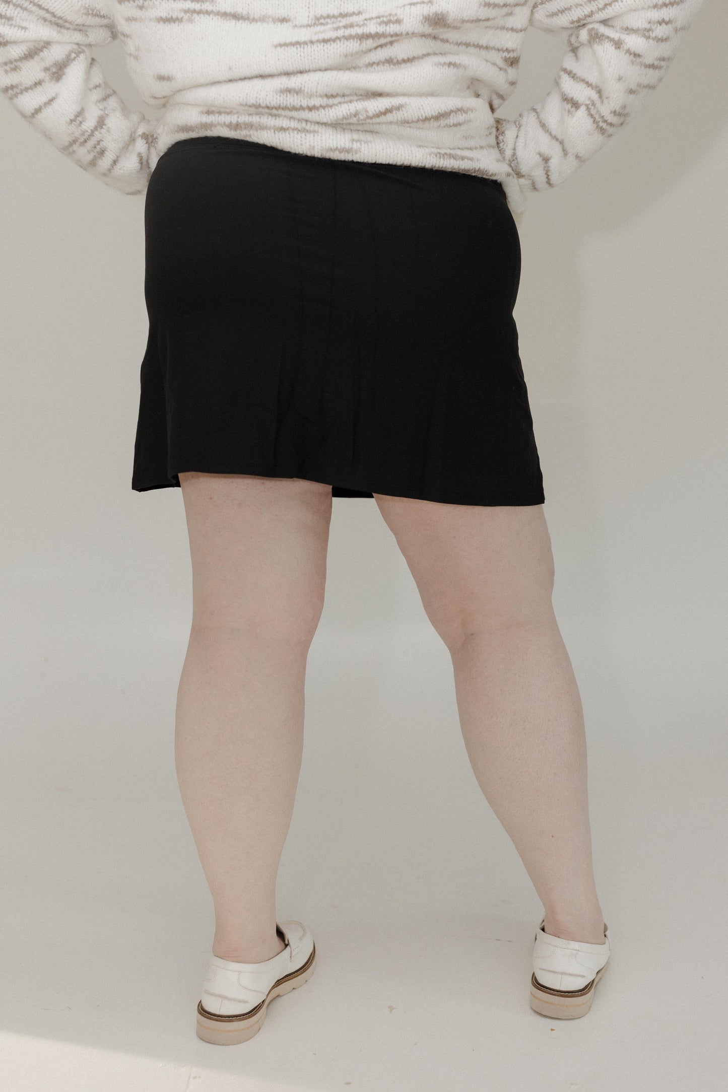 Person wearing a black skirt and white shoes on a plain background