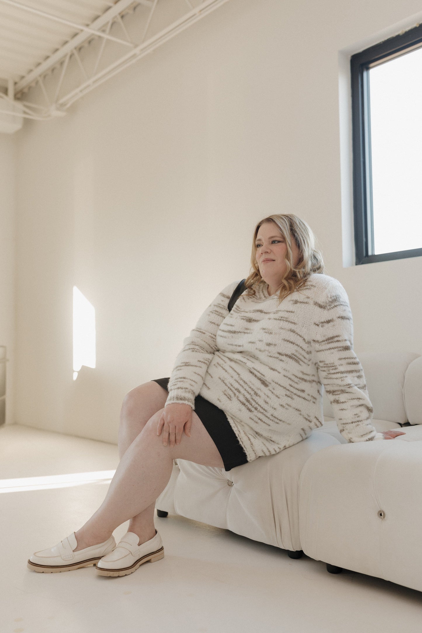Woman sitting on a white couch in a bright, minimalistic room.