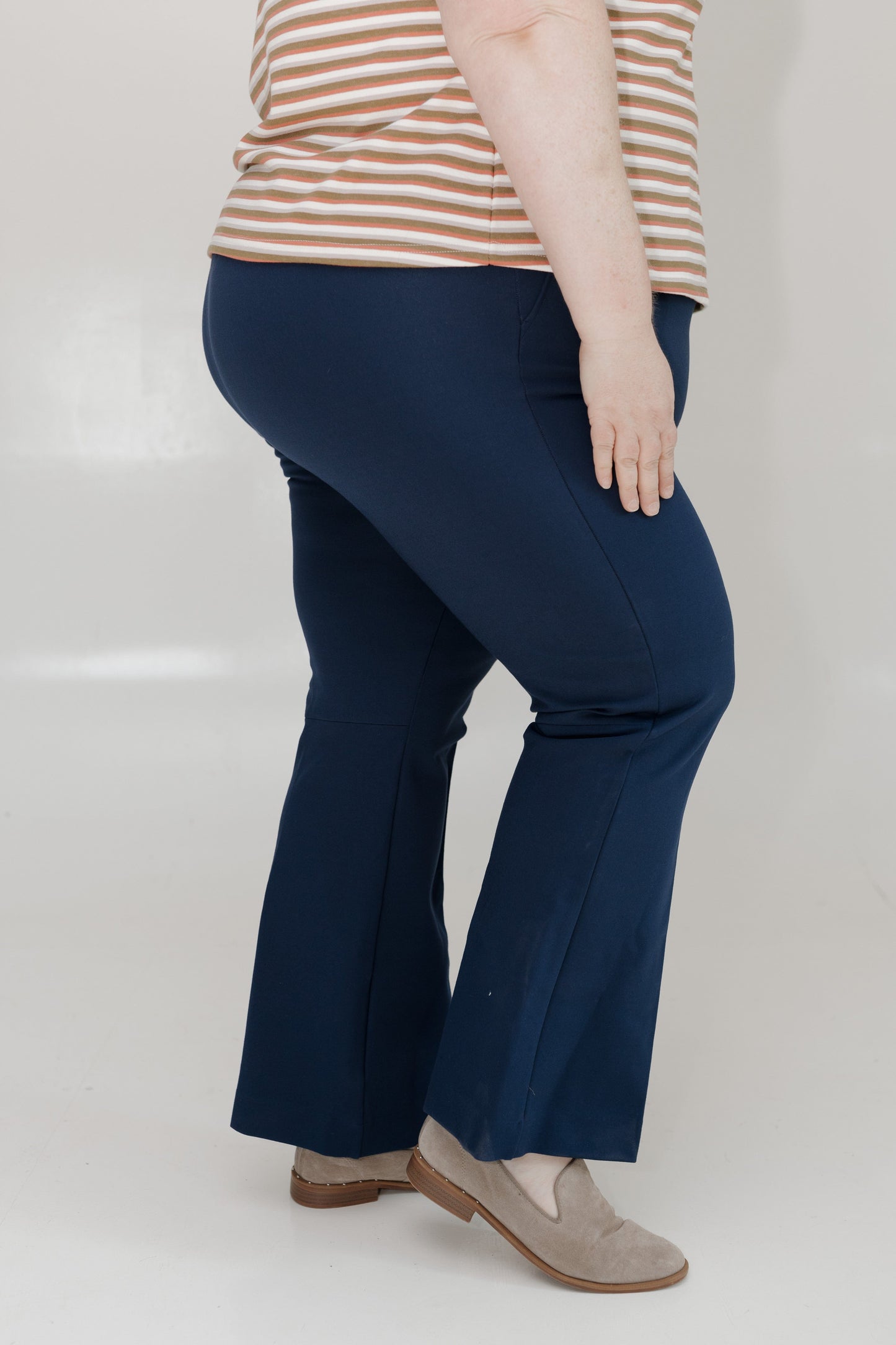Person wearing navy blue flared pants and a striped shirt on a white background