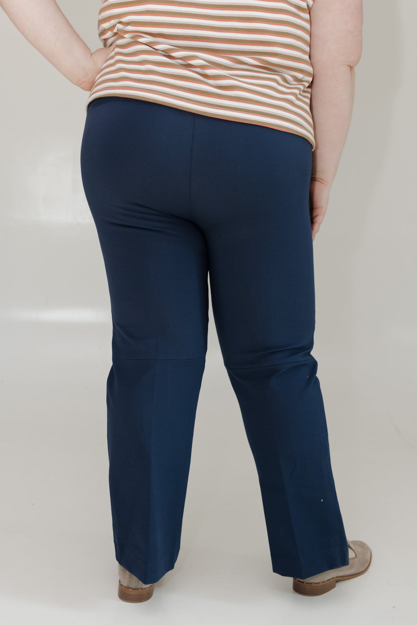 Person wearing navy blue pants and a striped shirt on a plain background