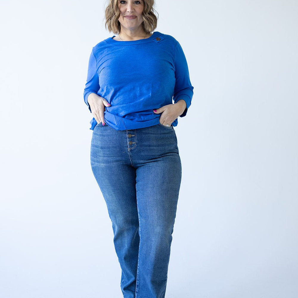 A person wearing a blue long-sleeve shirt and high-rise jeans stands against a plain white background.