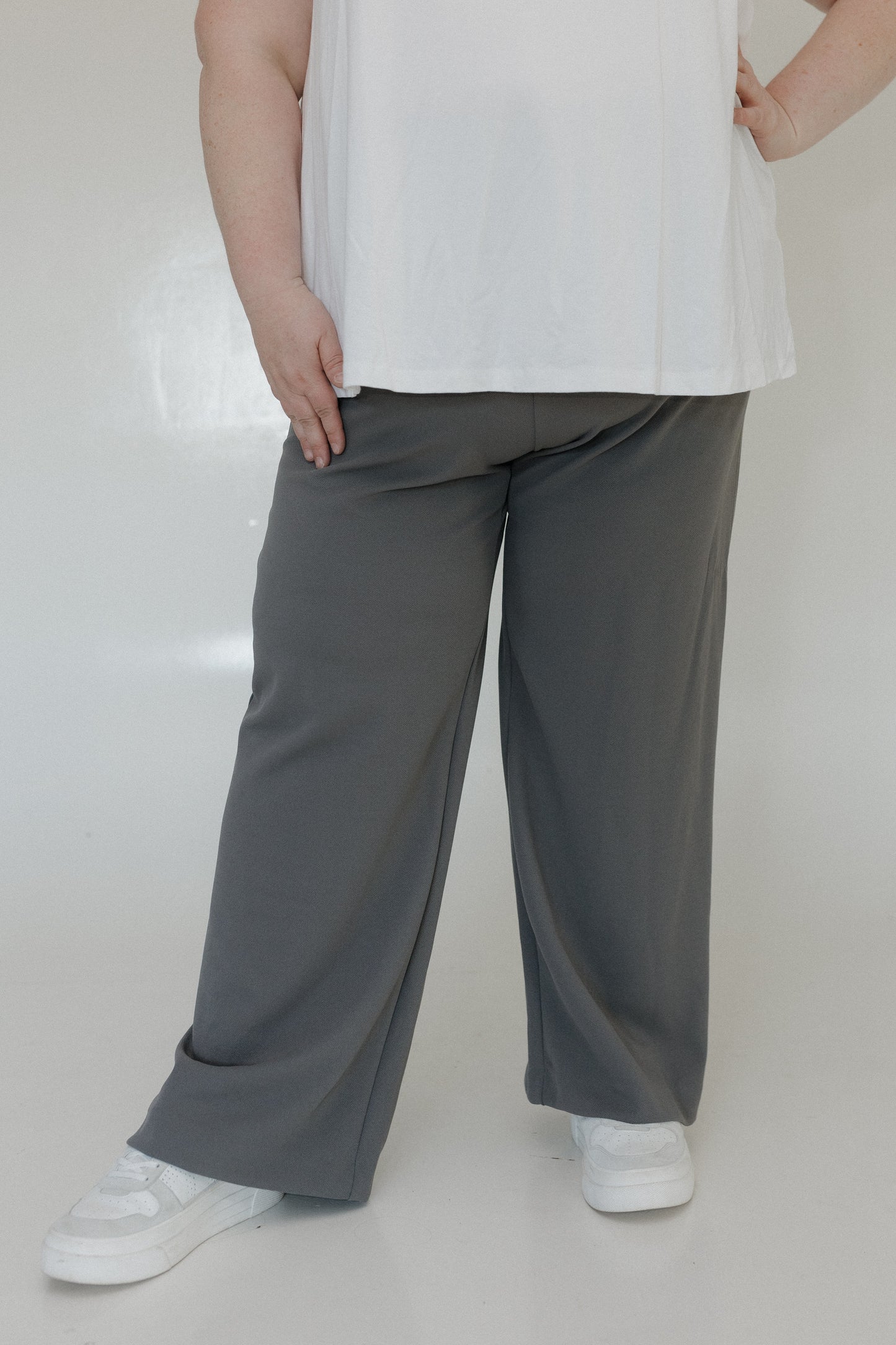 Person wearing a white top and gray wide-leg pants on a plain background