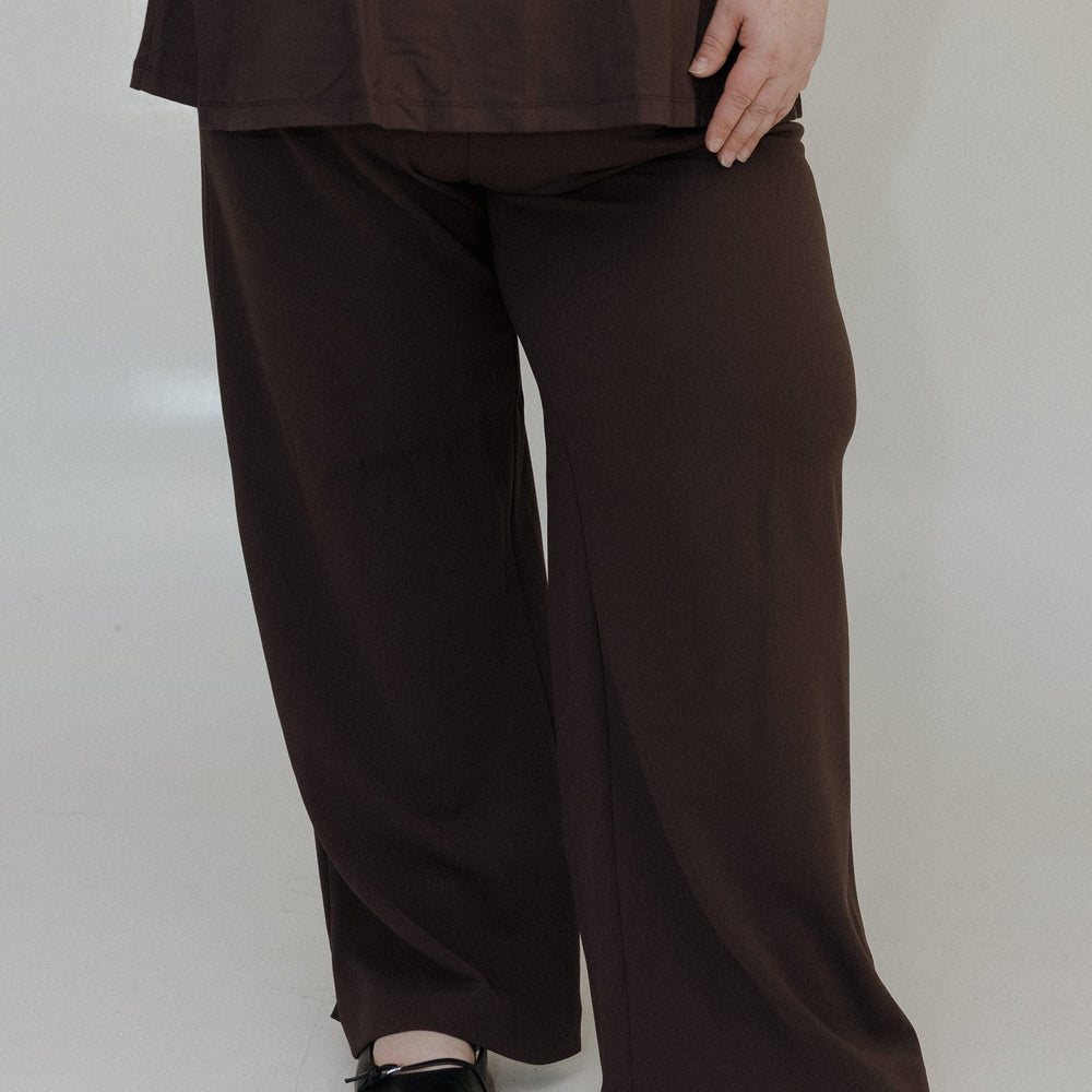 Person wearing brown wide-leg pants and a matching top on a white background
