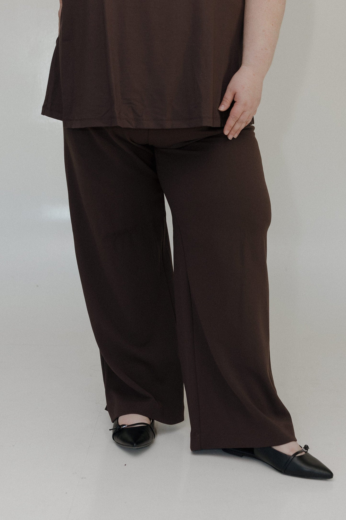 Person wearing brown wide-leg pants and a matching top on a white background
