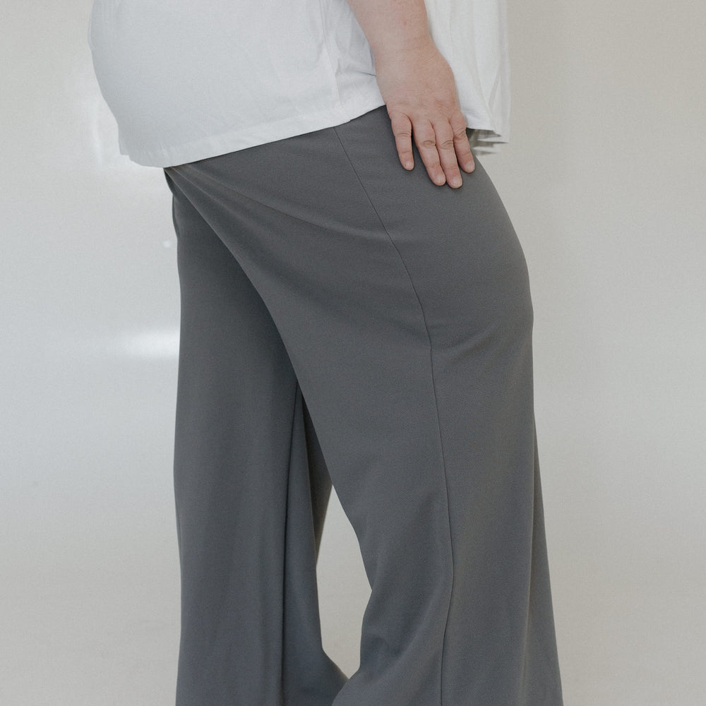 Person wearing gray wide-leg pants and a white top on a plain background