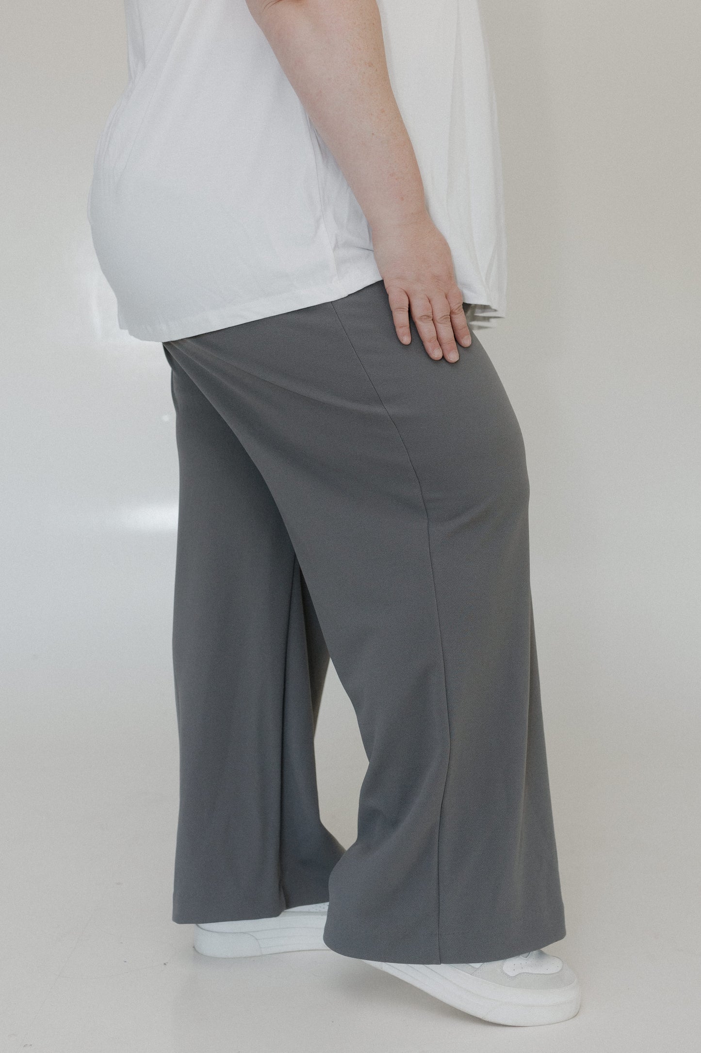 Person wearing gray wide-leg pants and a white top on a plain background