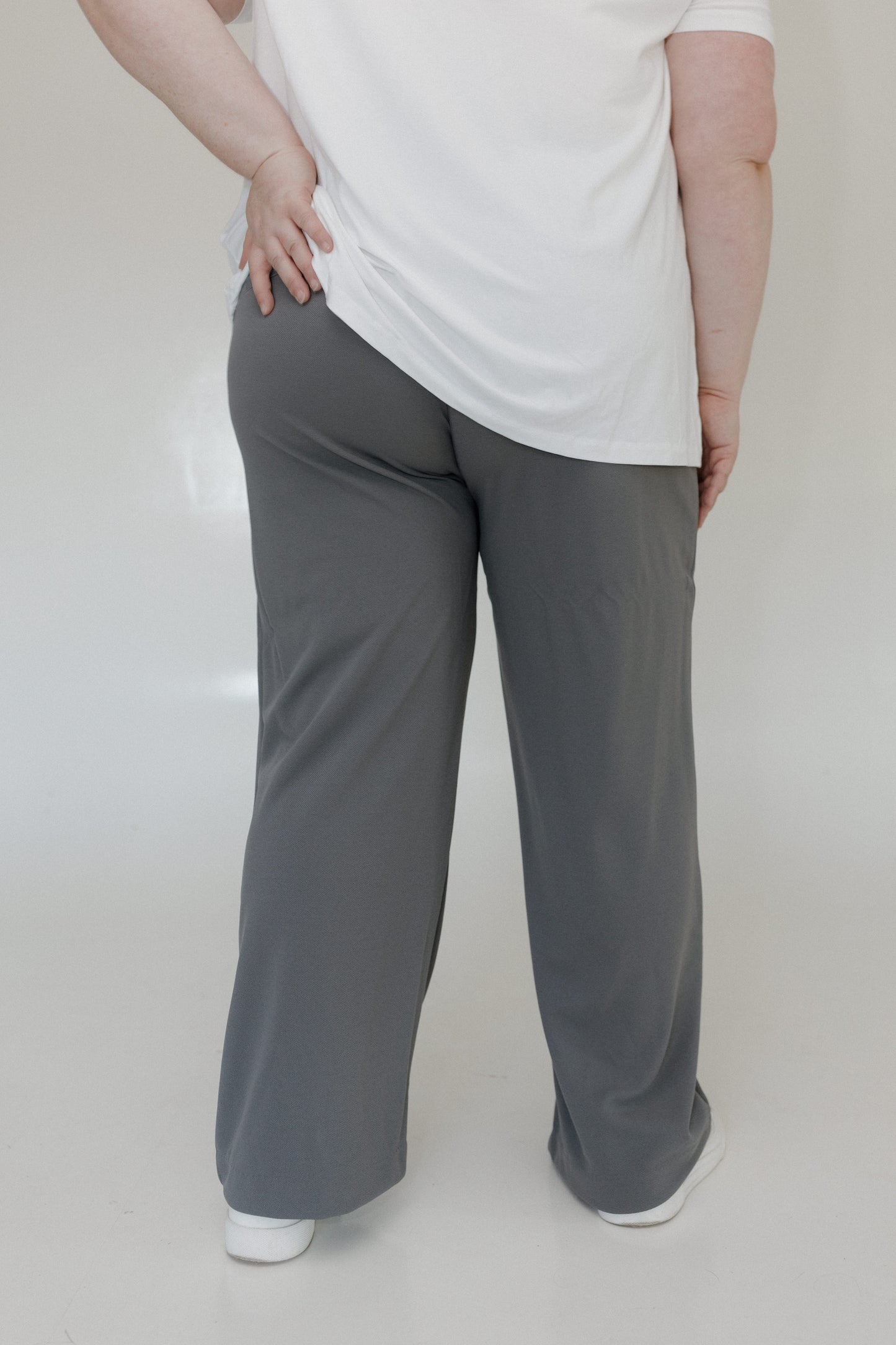 Person wearing gray pants and a white top on a plain background
