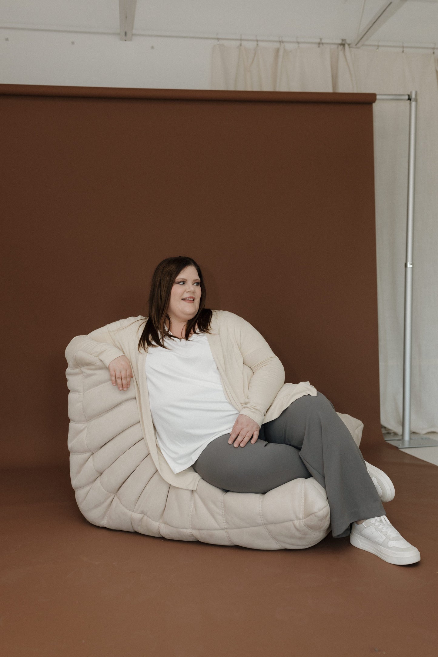 Person sitting on a large bean bag chair against a brown wall.