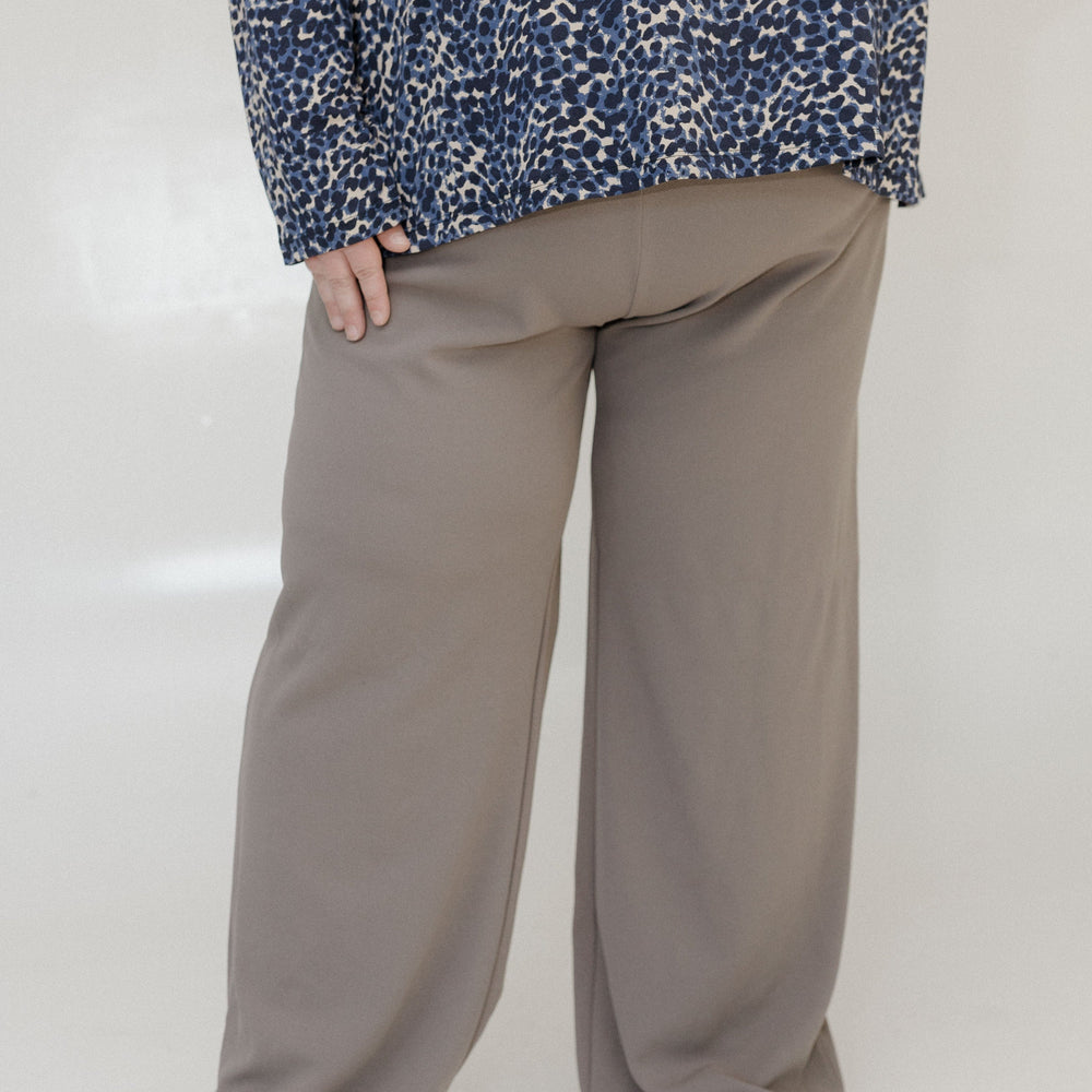 Person wearing a blue patterned top and beige wide-leg pants on a white background