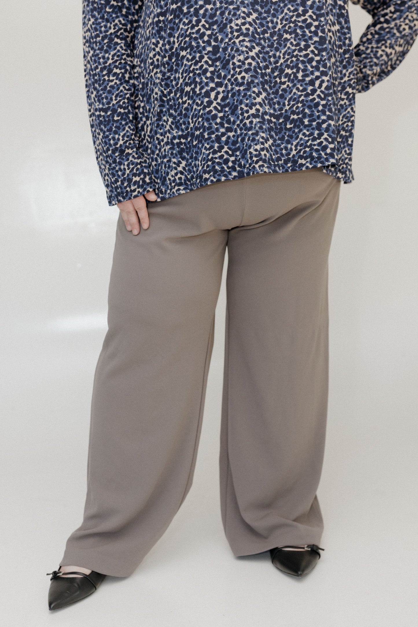 Person wearing a blue patterned top and beige wide-leg pants on a white background