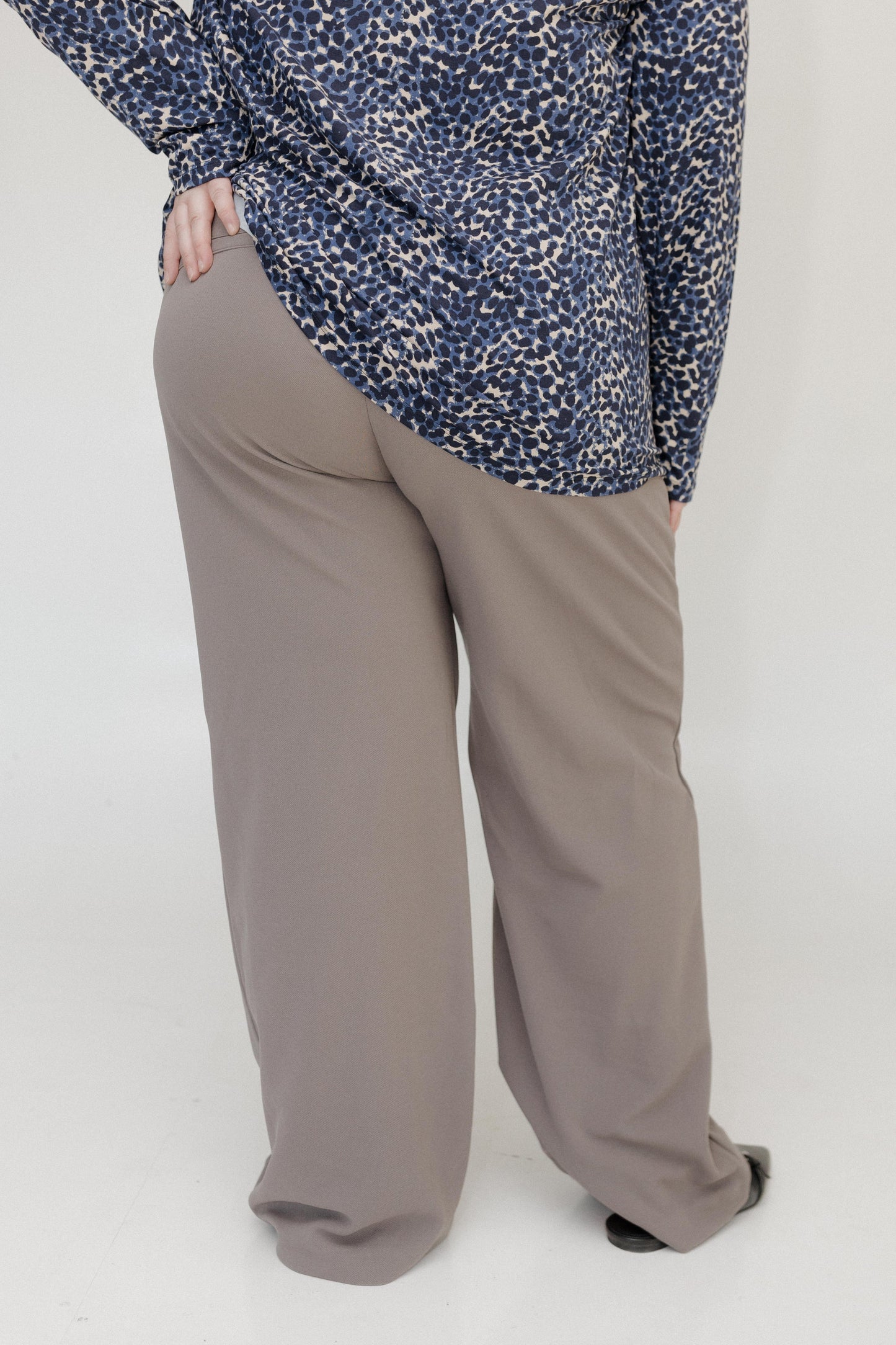 Person wearing a blue patterned top and beige pants on a white background