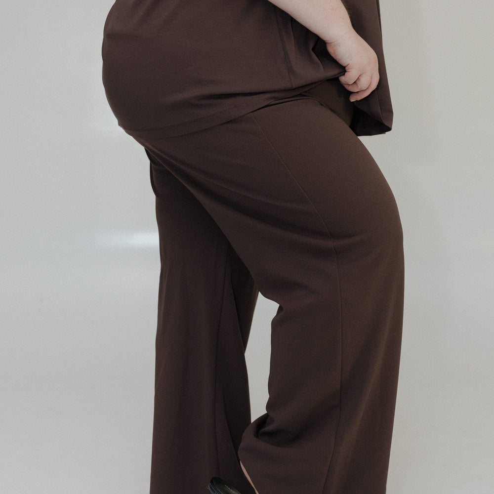 Person wearing a brown outfit with wide-leg pants on a plain background