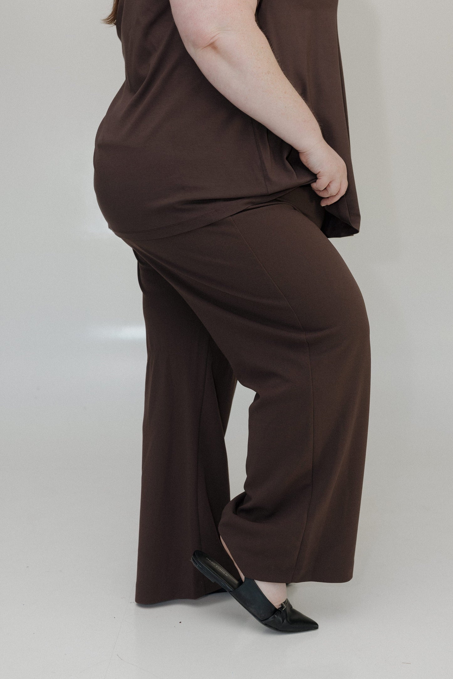 Person wearing a brown outfit with wide-leg pants on a plain background