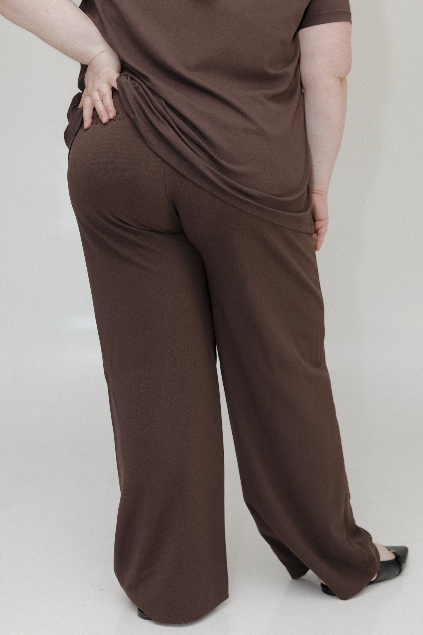 Person wearing a brown outfit with wide-leg pants on a plain background